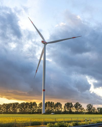 A large wind turbine standing alone in a field near a road under dramatic cloudy skies, symbolizing green energy and sustainable solutions.